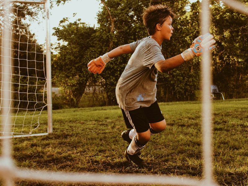 Young goalkeeper in gloves leaping across the goal